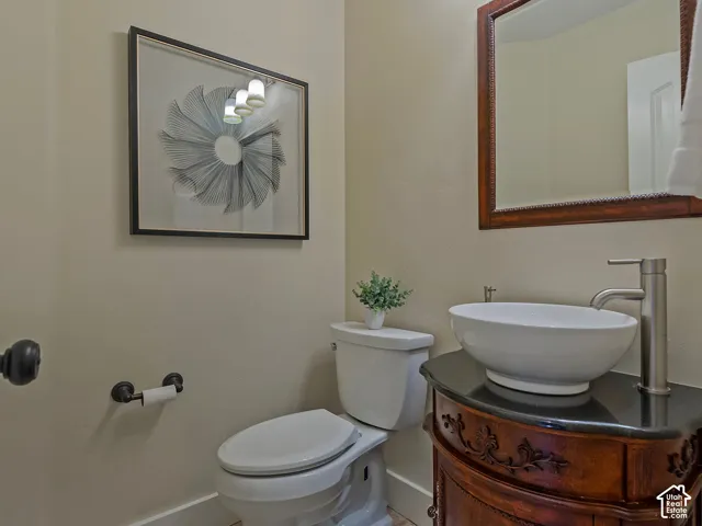 Vanity with a vessel sink, tall brushed nickel faucet, dark countertop, and decorative wood-finish base