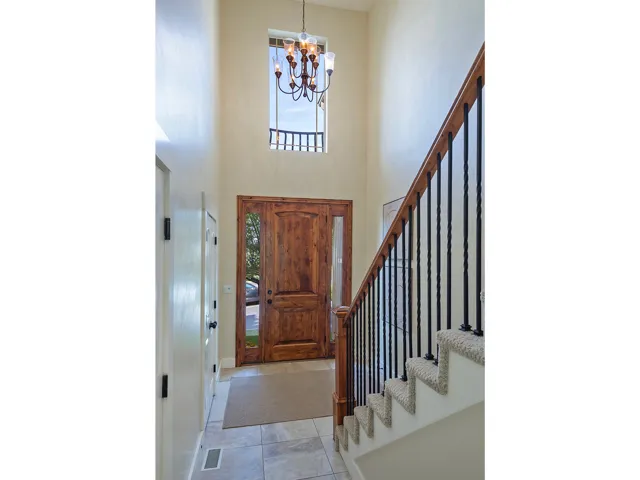 Two-story foyer featuring a wood-panel entry door with sidelights, a wrought iron chandelier, a staircase with carpeted treads and wrought iron balusters, and tile flooring