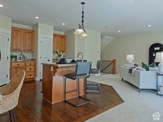 Kitchen island with seating, pendant lighting, wood-finish flooring, and recessed lighting