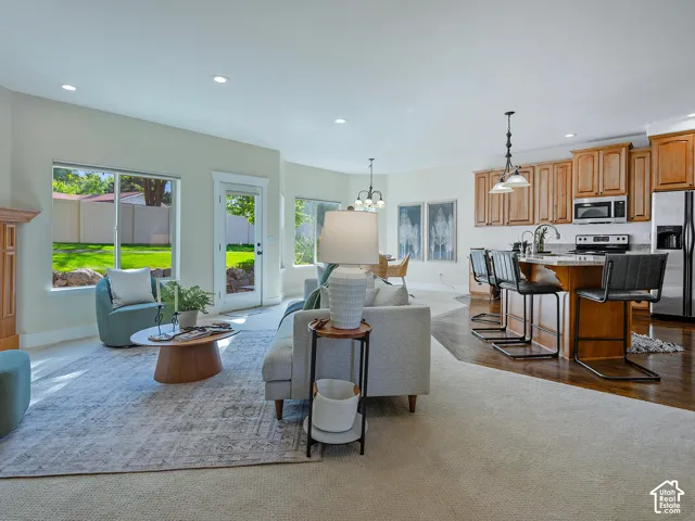 Open concept living area featuring a fireplace with wood mantel, ample natural light, a kitchen island with seating, wood cabinetry, and stainless steel appliances