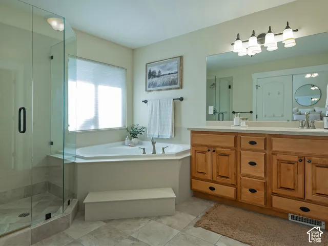 Glass-enclosed shower, corner soaking tub with built-in step, wood-finish vanity with countertop, large wall-mounted mirror, and tile flooring