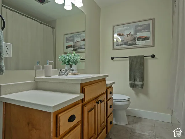 Bathroom featuring a vanity with light-colored countertops, a single basin sink, a wall-mounted mirror, and tile flooring