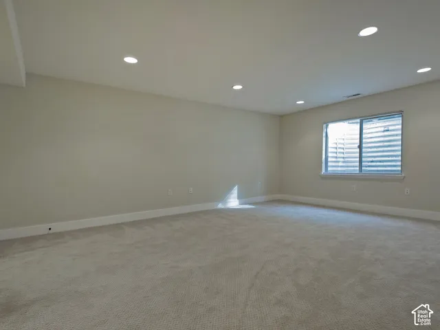Recessed ceiling lighting, light gray wall paint, white trim, light gray carpet, and a window with a window well