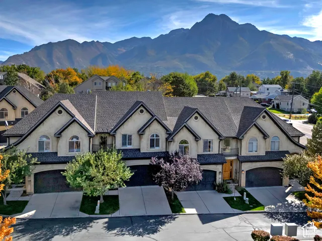 Mountain backdrop with a multi-unit property featuring stucco exteriors and dark shingle roofing