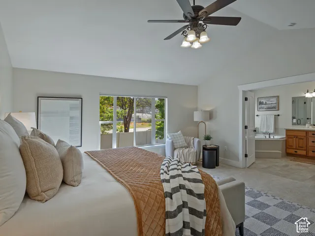 Vaulted ceiling with a ceiling fan light fixture, large window with natural light, attached three-panel door, built-in soaking tub, and a vanity with a double mirror