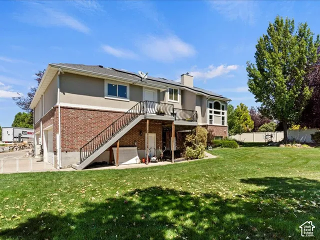 Expansive backyard with a manicured lawn, mature trees, multi-level exterior, and a second-story balcony with metal railings