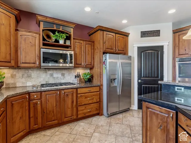 Wood cabinetry with decorative molding, dark stone countertops, stainless steel appliances, tiled flooring, and a tiled backsplash