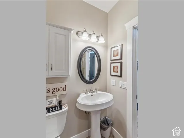 White pedestal sink with a chrome faucet, oval mirror, and wall-mounted light fixture