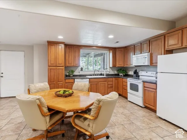 Kitchen featuring wood cabinetry, dark countertops, white appliances, and tiled flooring
