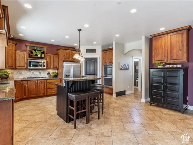 Spacious kitchen featuring warm wood cabinetry, a central island with bar seating, stainless steel appliances, and tile flooring