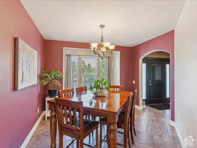 Recessed window with blinds, tiled flooring, arched doorway, and overhead chandelier
