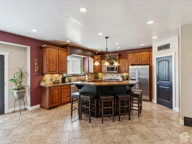 Spacious kitchen featuring warm wood cabinetry, stone-finish countertops, stainless steel appliances, a large center island, and tile flooring