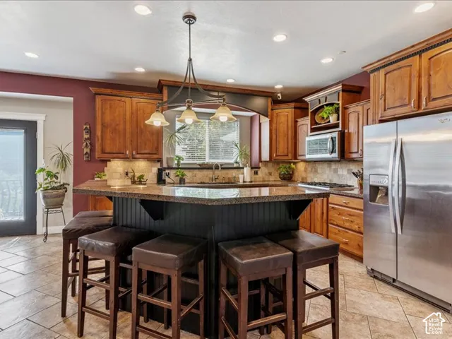 Spacious kitchen featuring an expansive island with seating, recessed lighting, wood cabinetry, stainless steel refrigerator, and tiled flooring