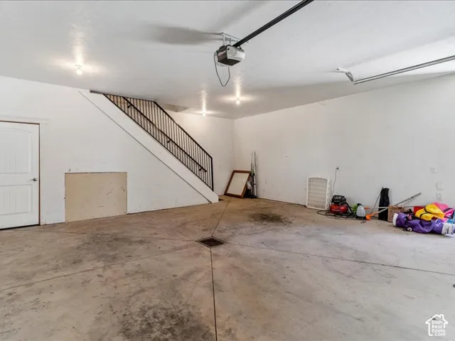 Spacious garage featuring a concrete floor, built-in staircase with metal railing, recessed lighting, and a paneled entry door