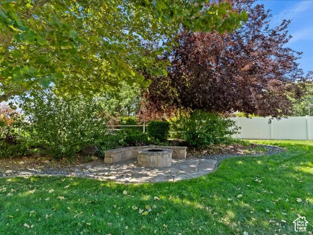 Expansive green lawn with a flagstone patio featuring a built-in fire pit and stone seating