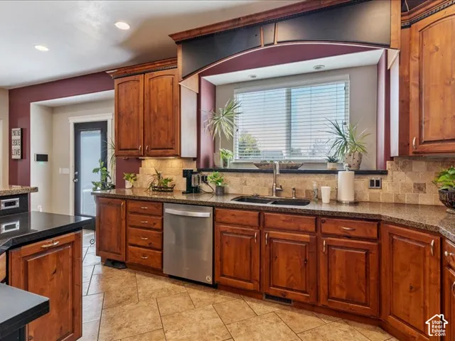 Wood cabinetry, stone countertops, stainless steel dishwasher, tile backsplash, and tile flooring