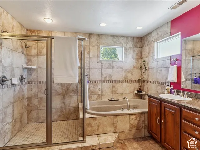 Tiled bathroom featuring a glass-enclosed shower, a built-in soaking tub, a single vanity with an undermount sink, and recessed lighting