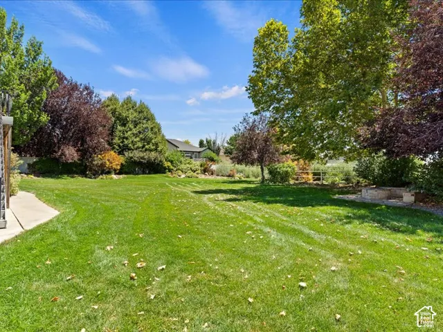 Expansive lawn with mature trees, established landscaping, and a built-in stone fire pit