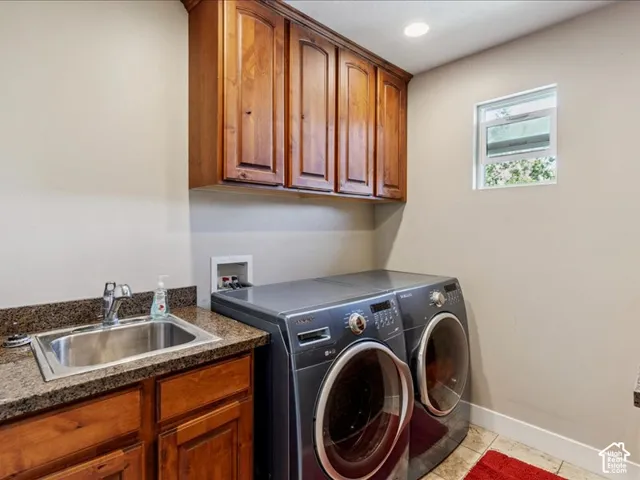 Dedicated laundry room featuring rich wood cabinetry with ample storage, granite-style countertop with stainless steel sink, high-efficiency front-load washer and dryer with large-capacity drums, recessed lighting, and a small window for natural light