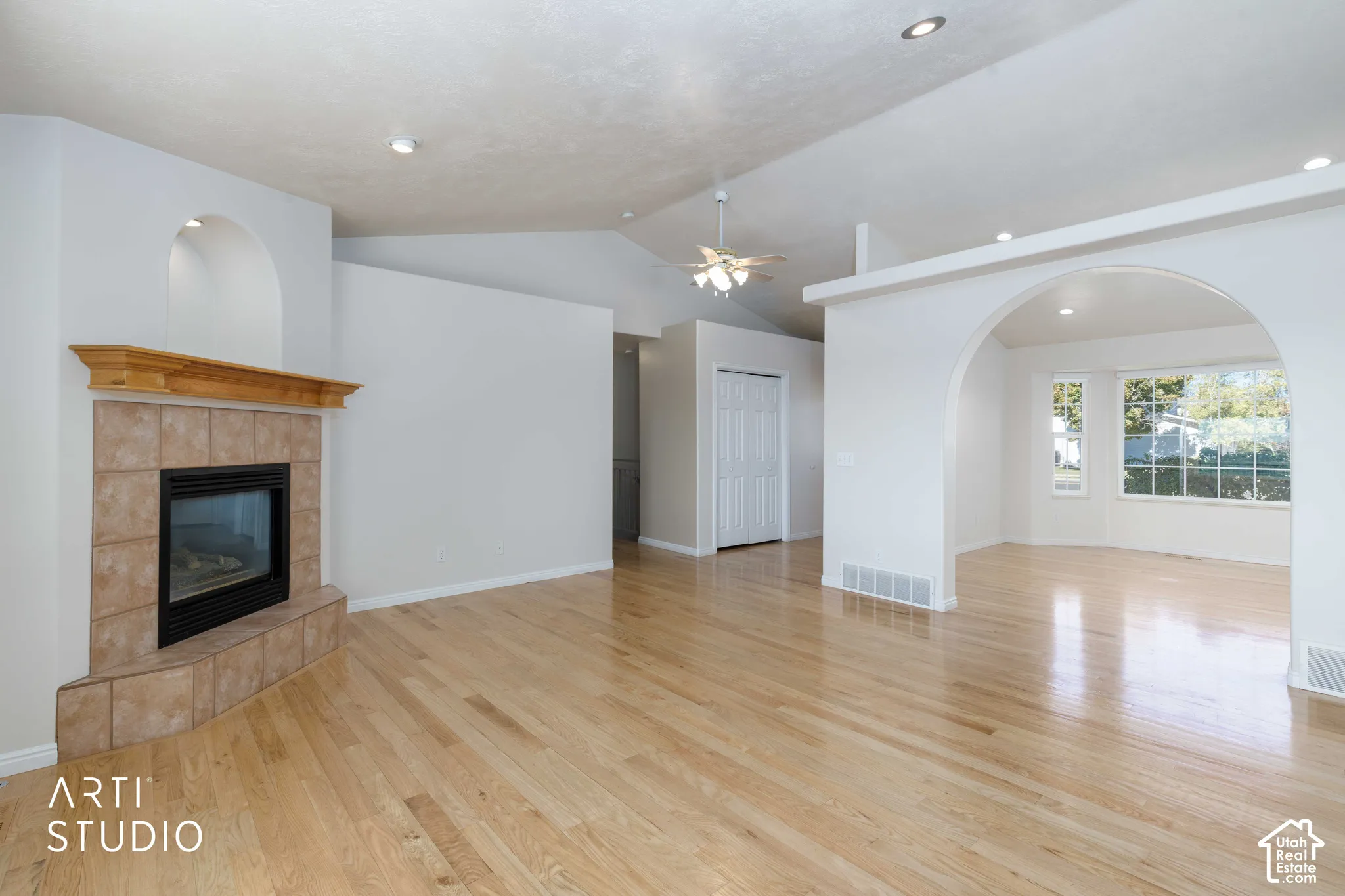Hardwood flooring, tiled fireplace with wooden mantel, vaulted ceiling with ceiling fan, recessed lighting, and an arched doorway