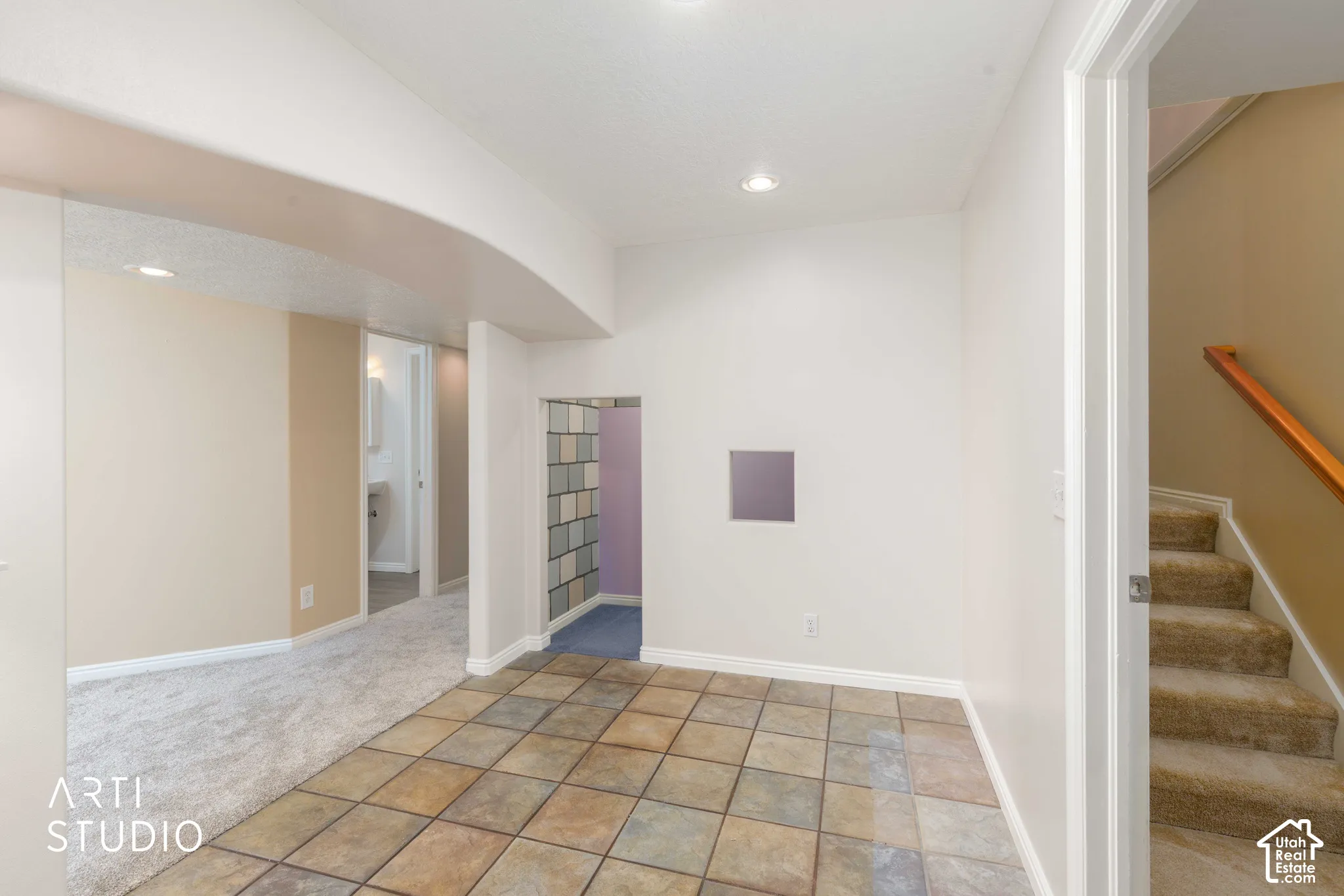 Tiled flooring with an arched entry, recessed lighting, and a carpeted staircase with a wood handrail