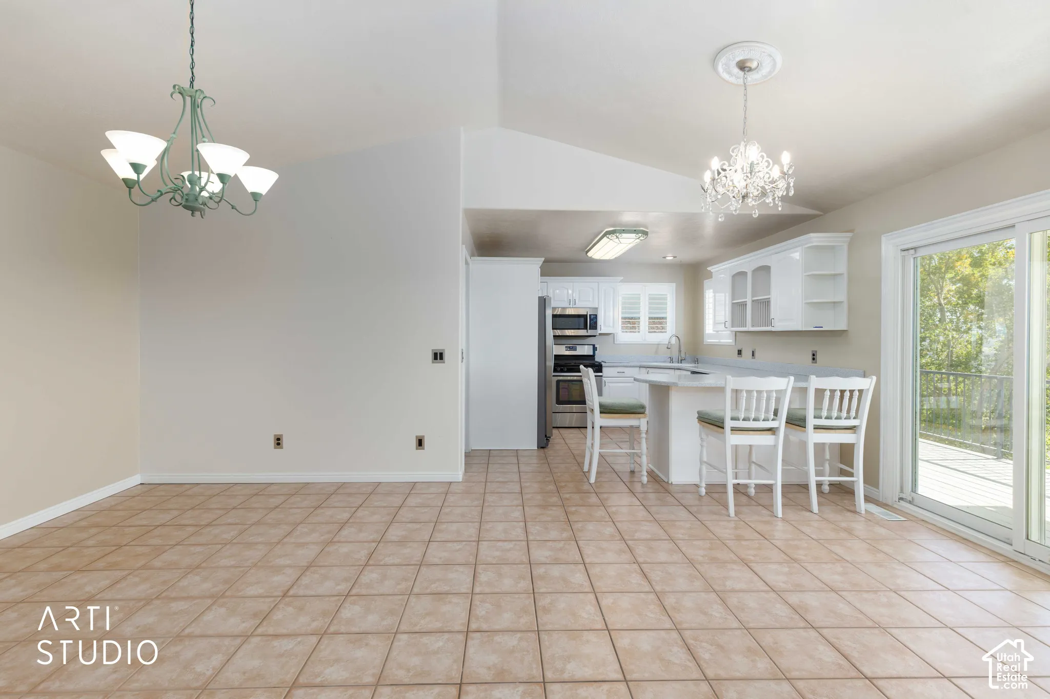 Open-concept living space featuring vaulted ceilings, tile flooring, a kitchen with white cabinetry, stainless steel appliances, and a sliding glass door leading to an exterior deck
