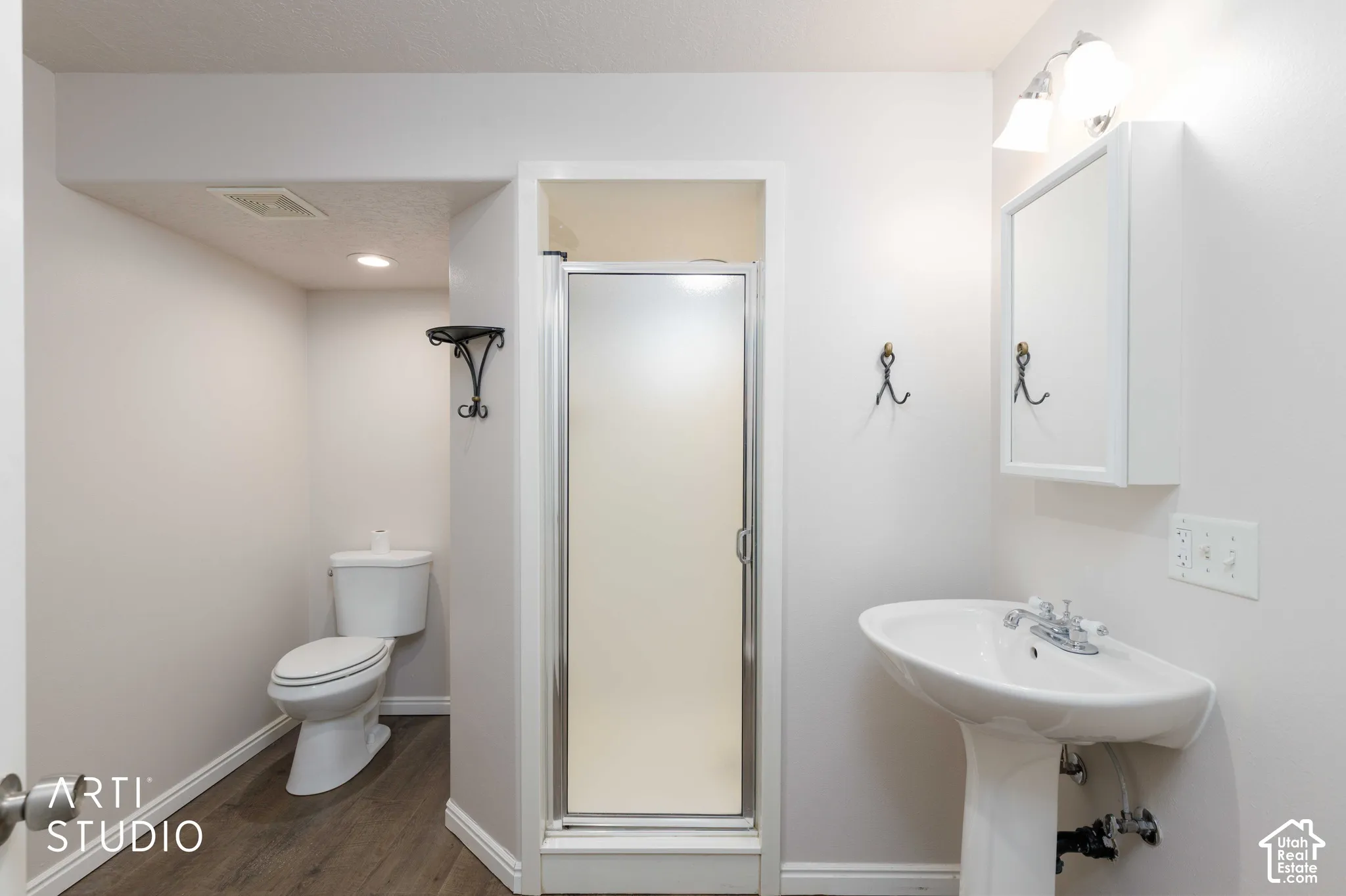 Pedestal sink with chrome fixtures, mirrored medicine cabinet, enclosed shower stall, and wood-finish flooring
