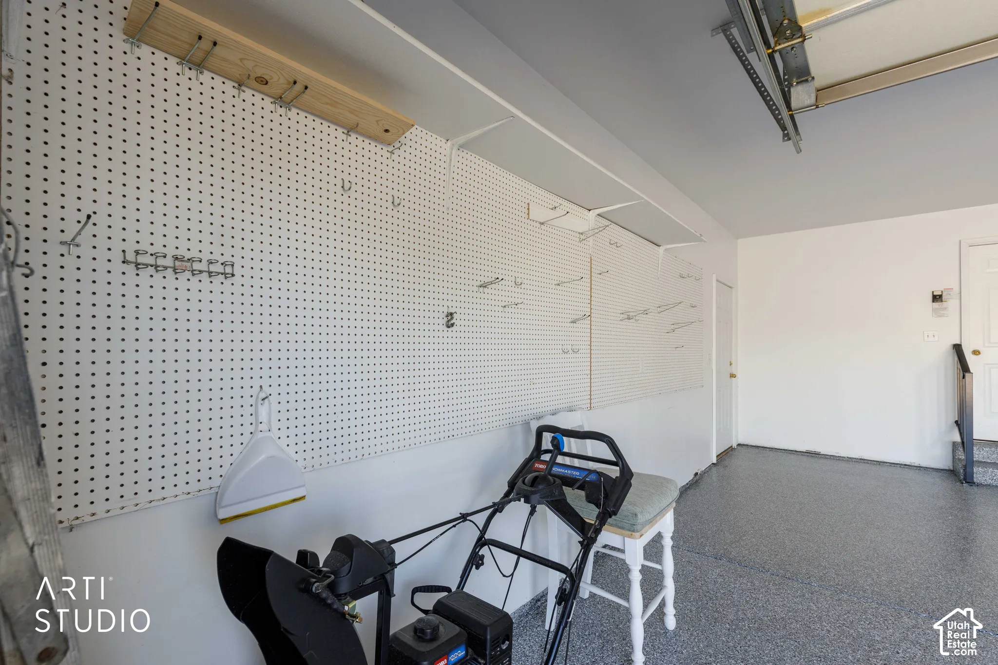 Garage with a speckled epoxy-coated floor, extensive pegboard wall storage, and overhead shelving