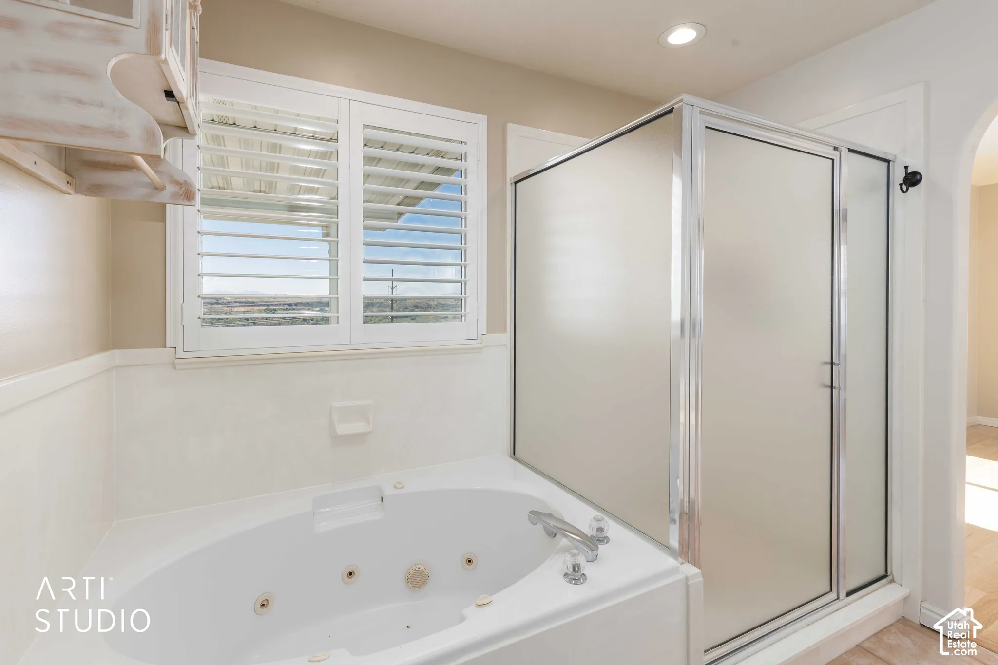 Jetted soaking tub, separate shower with frosted glass enclosure, window with plantation shutters, and recessed lighting