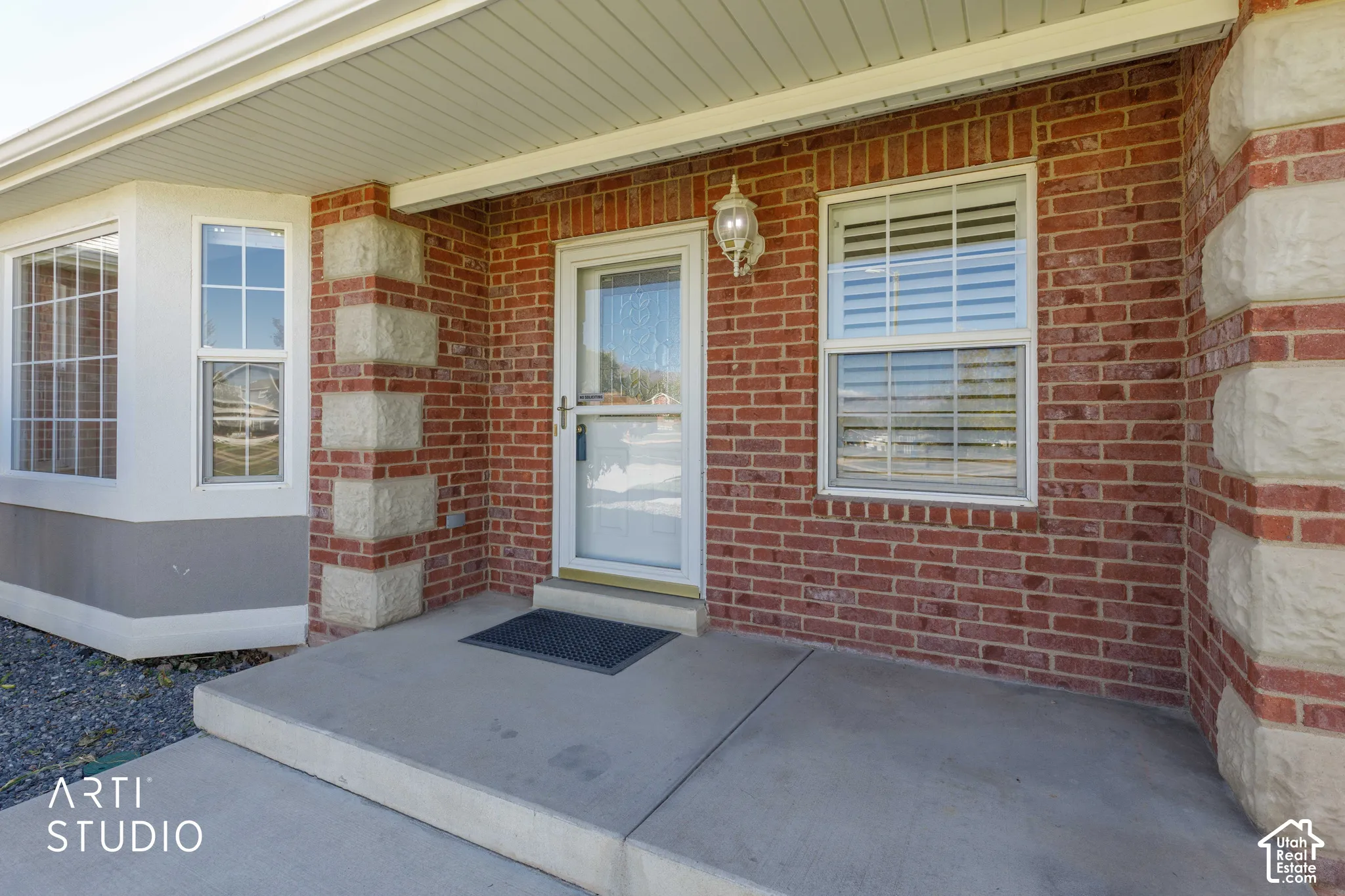 Brick facade with decorative stone accents, concrete porch, and a white entry door with a screen door