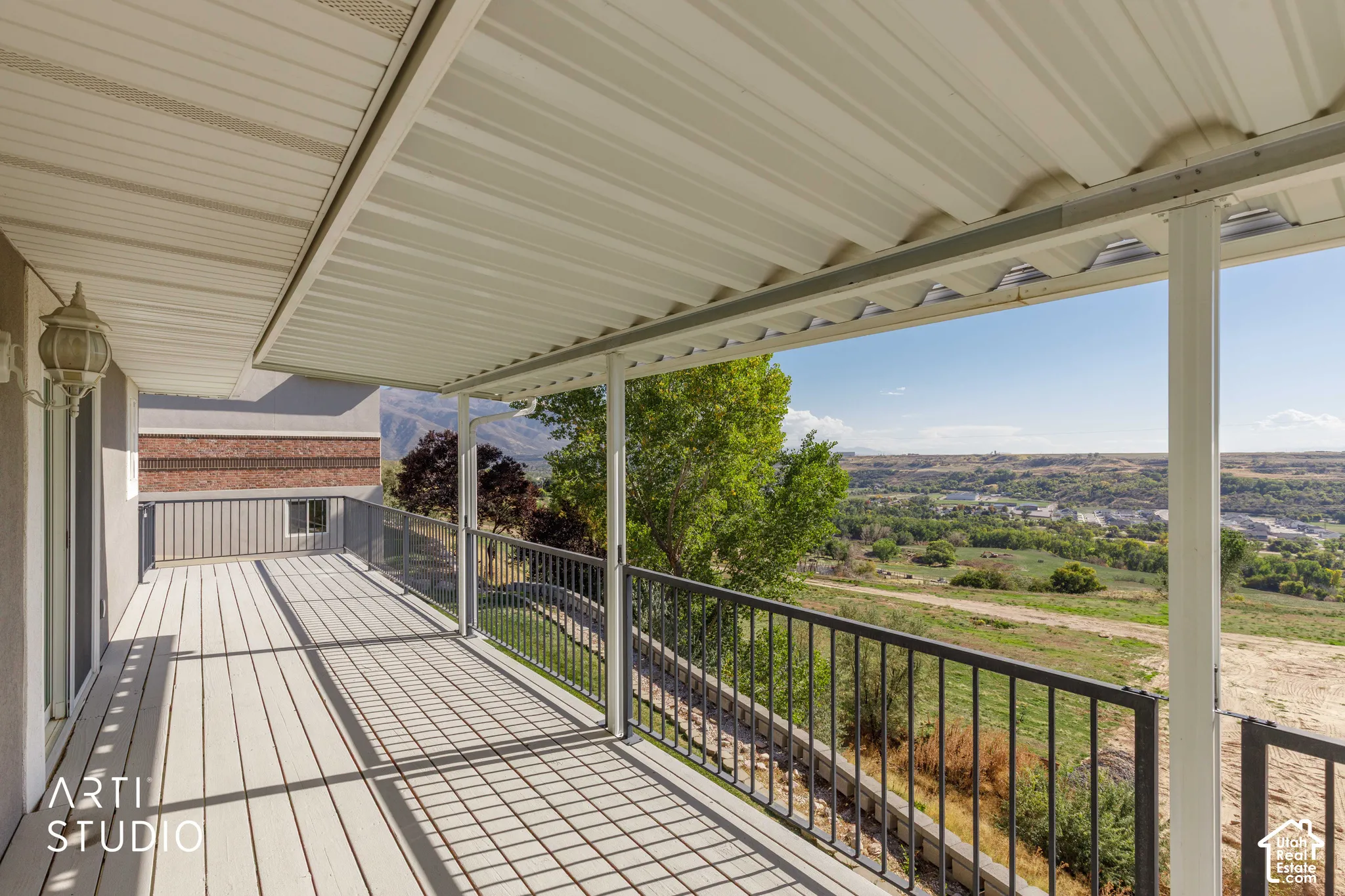 Covered outdoor deck with light-colored decking, metal railings, and a wall-mounted light fixture