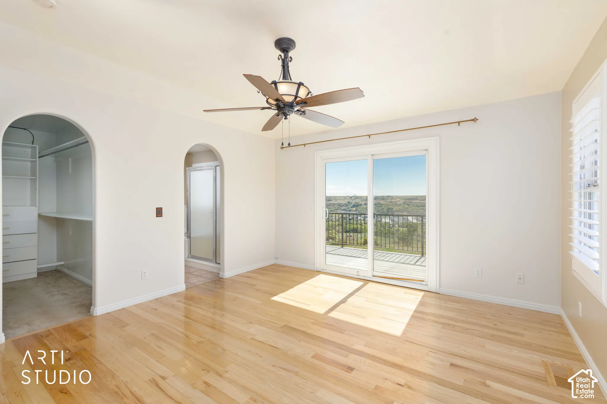 Hardwood flooring, arched doorways, built-in shelving, ceiling fan, and sliding glass door to balcony