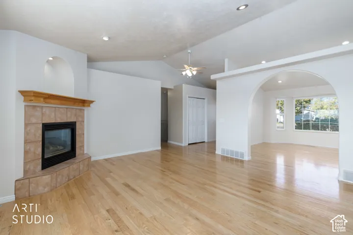 Hardwood flooring, tiled fireplace with wooden mantel, vaulted ceiling with ceiling fan, recessed lighting, and an arched doorway