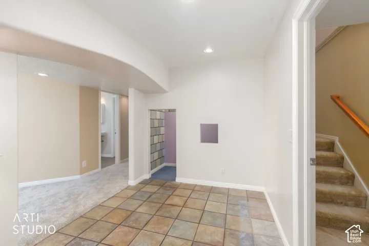 Tiled flooring with an arched entry, recessed lighting, and a carpeted staircase with a wood handrail