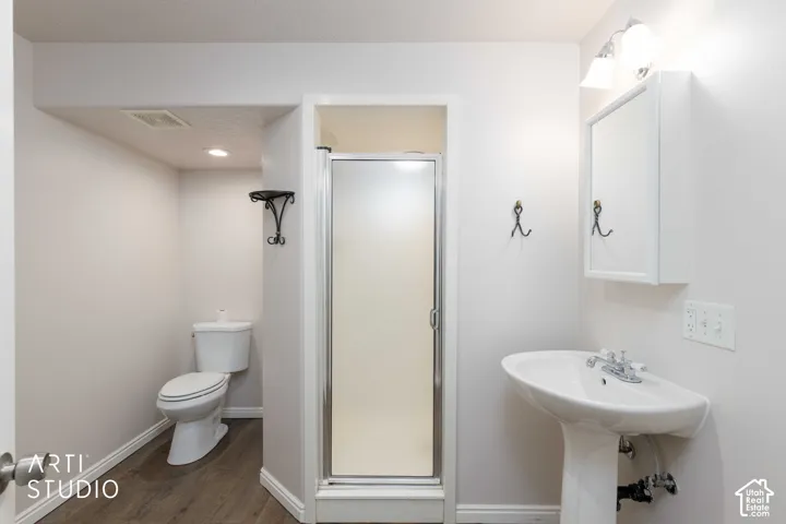Pedestal sink with chrome fixtures, mirrored medicine cabinet, enclosed shower stall, and wood-finish flooring