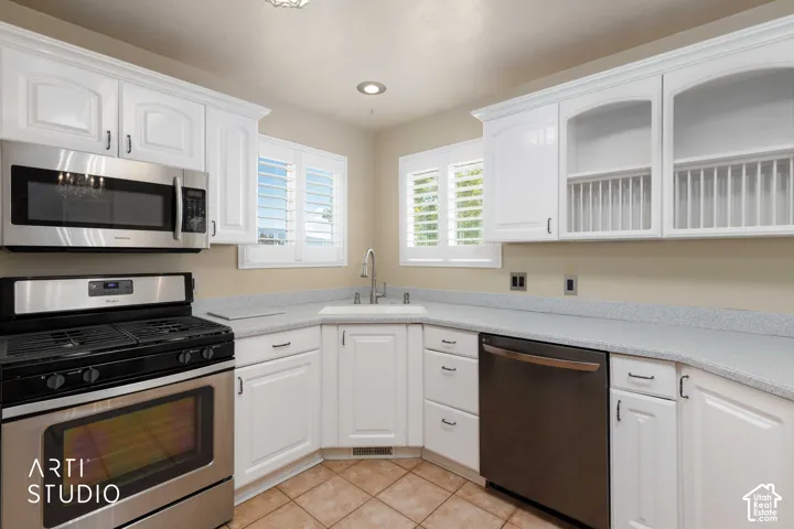White cabinetry, stainless steel appliances, corner sink, plantation shutters, and tile flooring