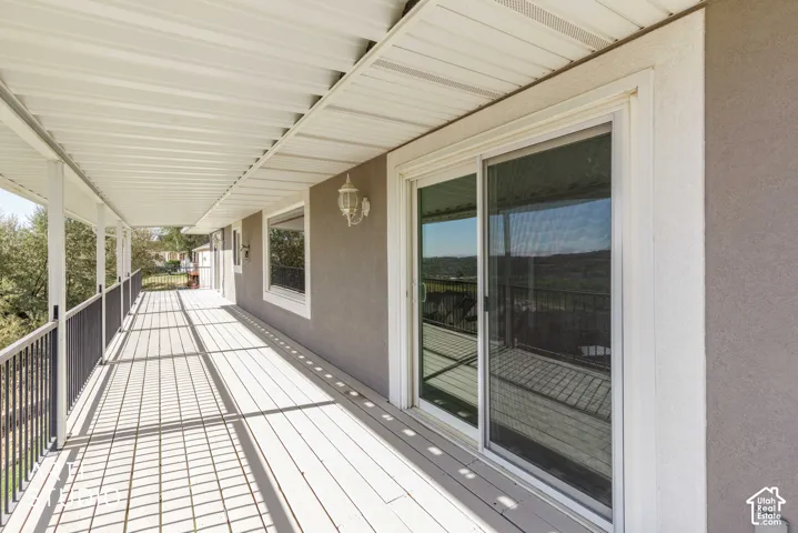 Covered outdoor deck with white painted wood-finish flooring, white ceiling, and gray exterior wall with a sliding glass door