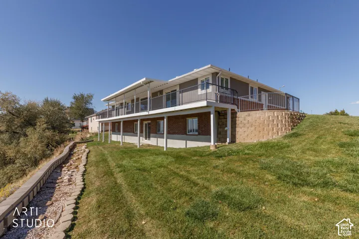 Multi-level exterior with a second-story covered balcony, a lower-level patio, and a retaining wall