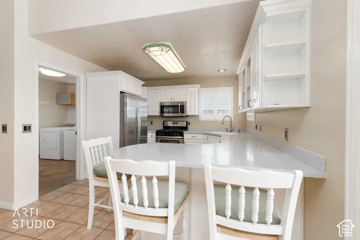 Kitchen featuring white cabinetry, stainless steel appliances, a breakfast bar, and tile flooring