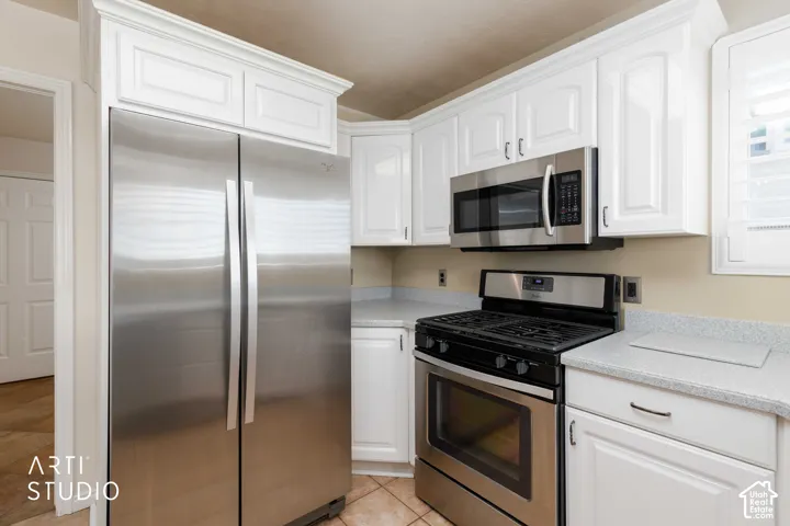 White cabinetry with crown molding, stainless steel appliances, speckled countertops, and tile flooring
