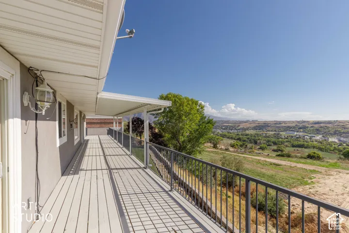 Expansive outdoor deck with a protective overhang, metal and glass railing, and distant natural scenery