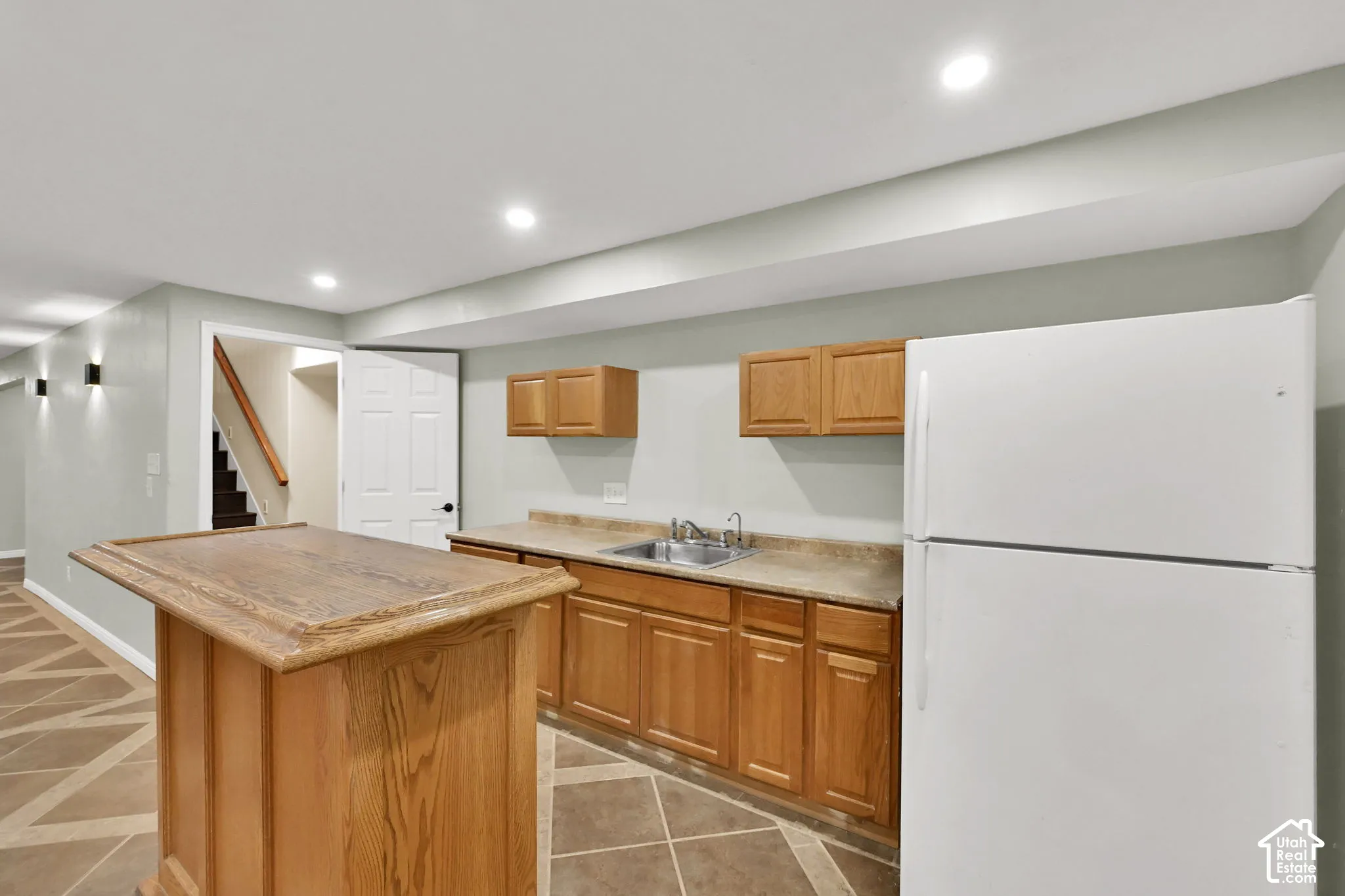 Basement wet bar featuring a wood-finish counter, accompanied by a full-size refrigerator.