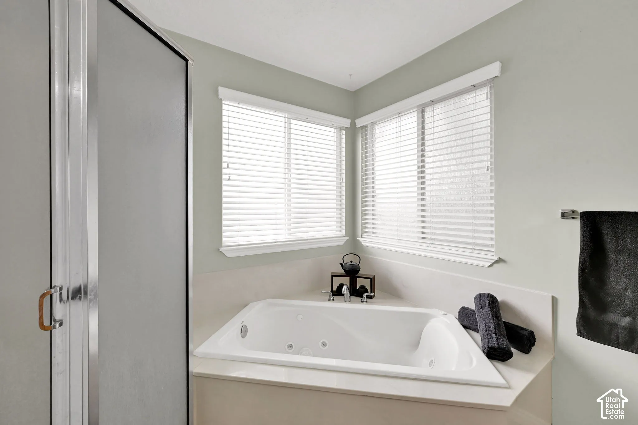 Corner soaking tub with integrated jets, dual windows with blinds, and an adjacent enclosed shower.