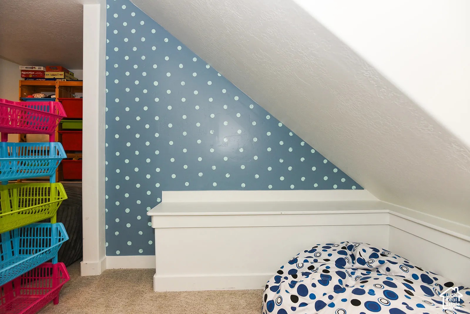 Carpeted flooring, angled ceiling, built-in storage bench, and a wall with a polka-dot pattern