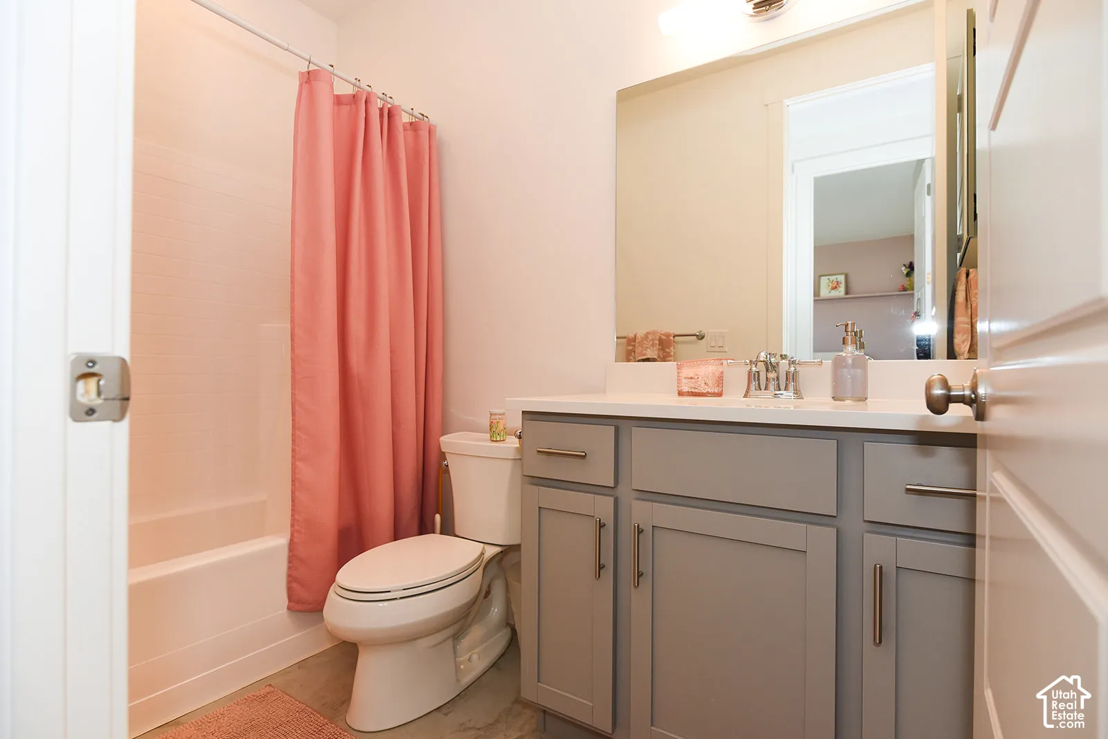 White single-piece bathtub, gray vanity cabinetry, white countertop, chrome faucet, and a large wall-mounted mirror