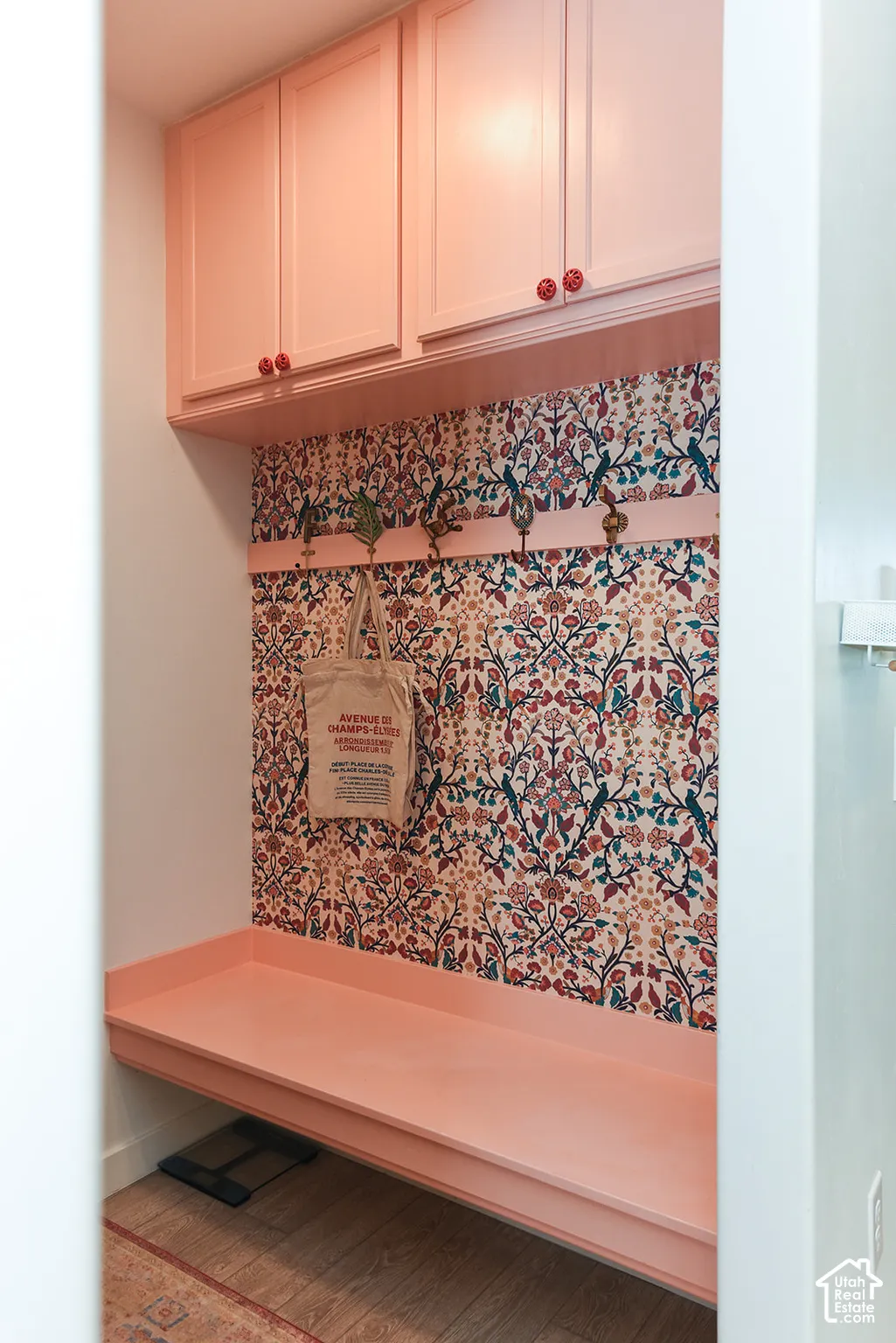 Built-in cabinetry with decorative hardware, patterned wall covering, bench seating, and wood-finish flooring