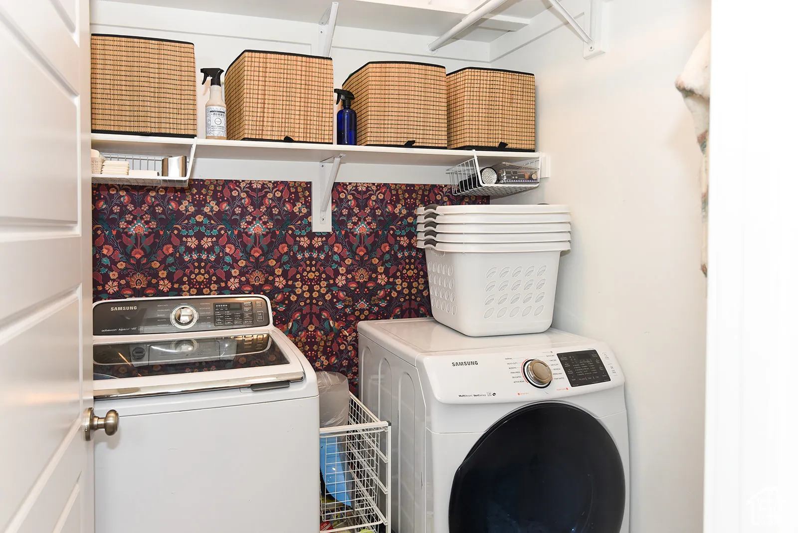 Laundry area featuring built-in shelving, patterned accent wall, and a white paneled door