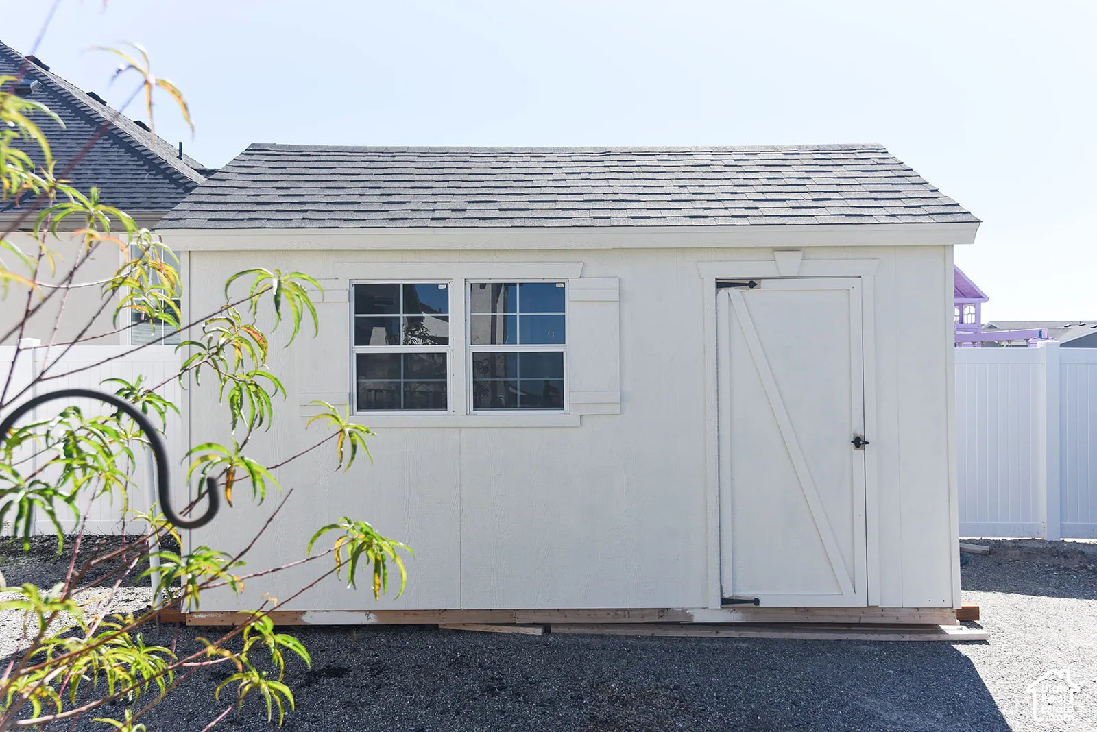 Utility shed featuring a gable roof, two windows with decorative shutters, and a single door with a dark handle