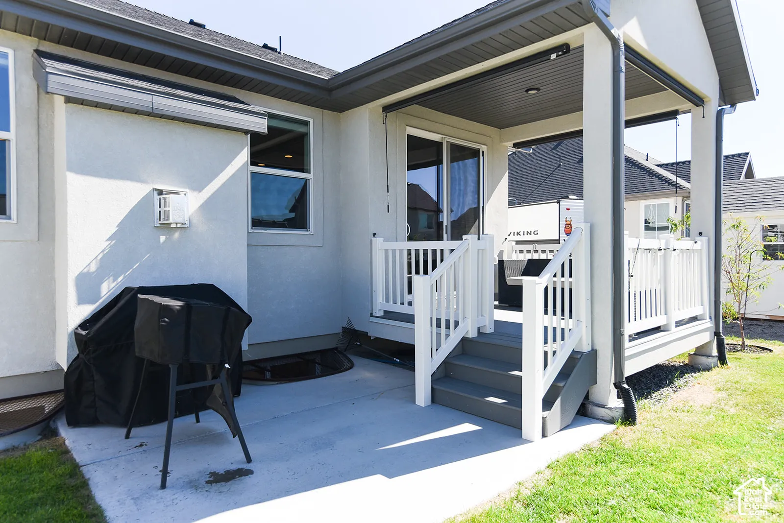 Covered patio with sliding glass door access, white railings, a concrete landing, and a manicured lawn area
