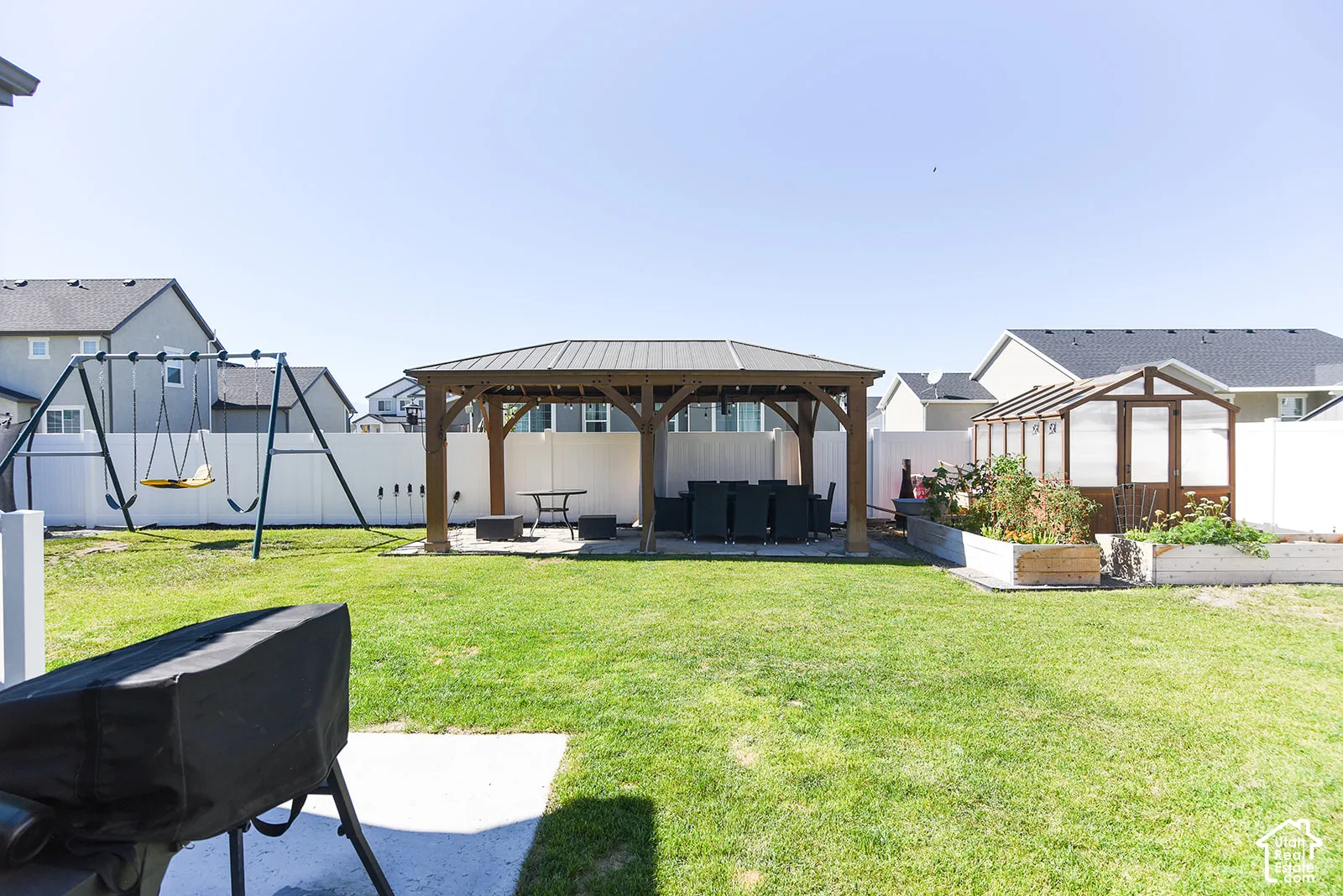 Expansive backyard featuring a large green lawn, a wooden gazebo with a metal roof, a wood-framed greenhouse, and raised garden beds